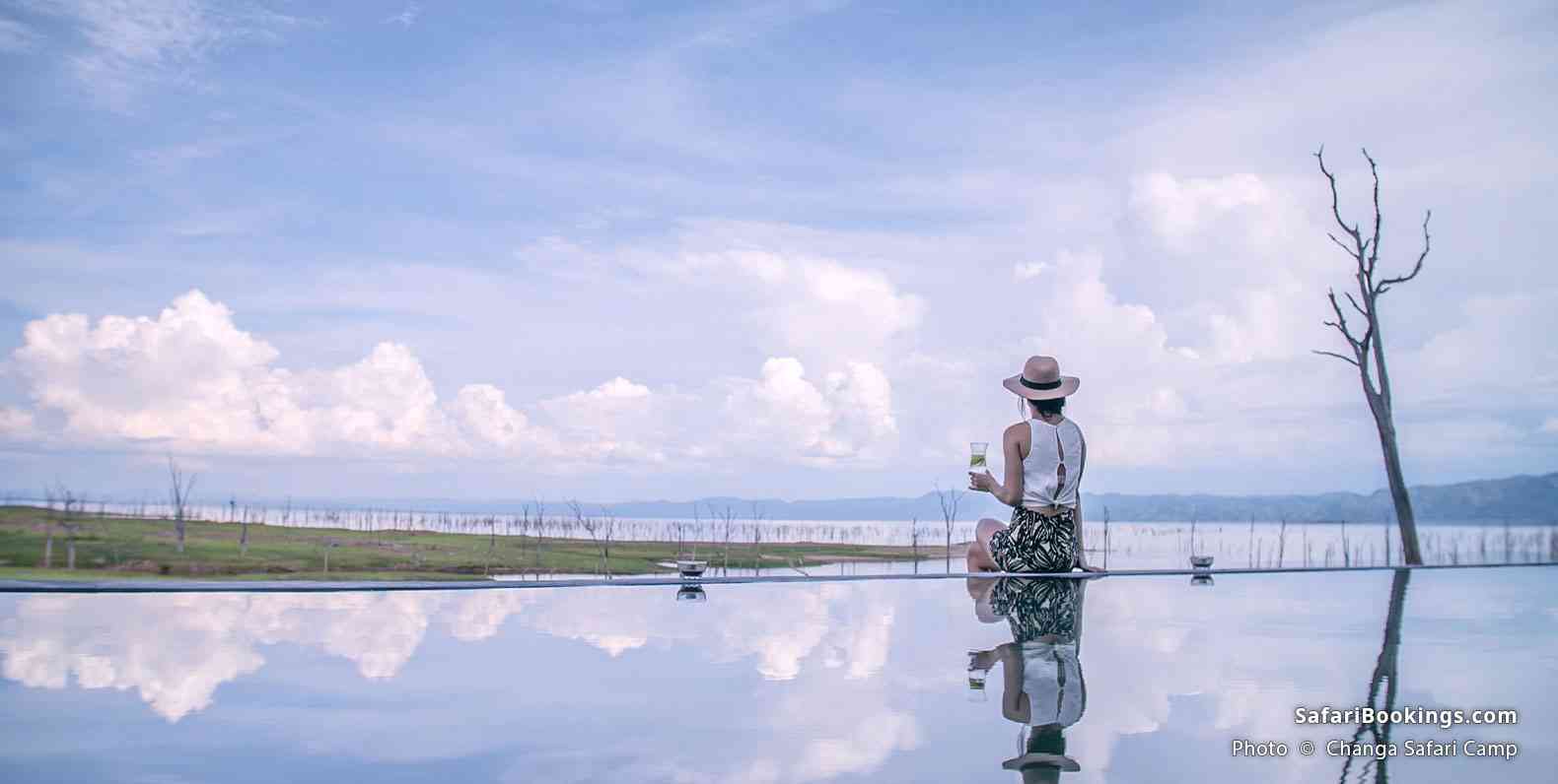 Woman in Changa Safari Camp, sitting by the pool and enjoying a drink and the view of the river