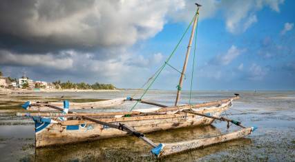 Traditional wooden dhow with outriggers on the beach at low tide in Jambiani